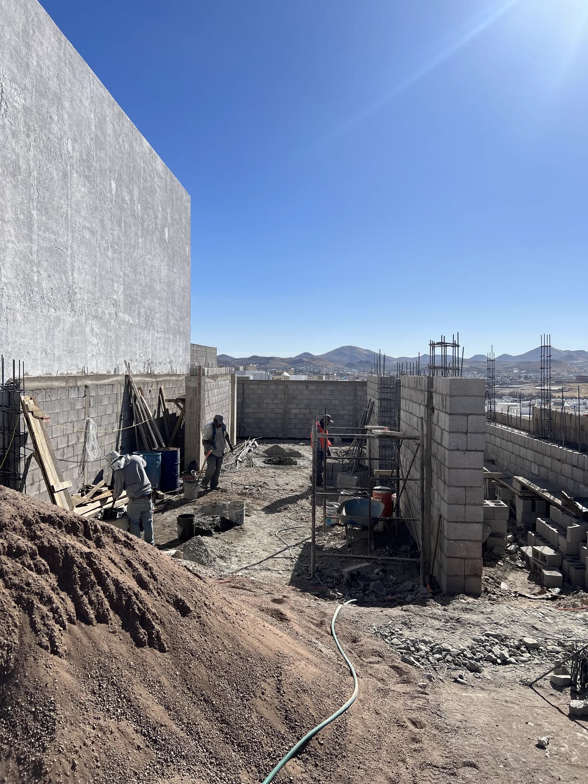 Obra de Casa Caleres con la cuadrilla levantando los muros de block, los castillos armados y la ciudad al fondo.
